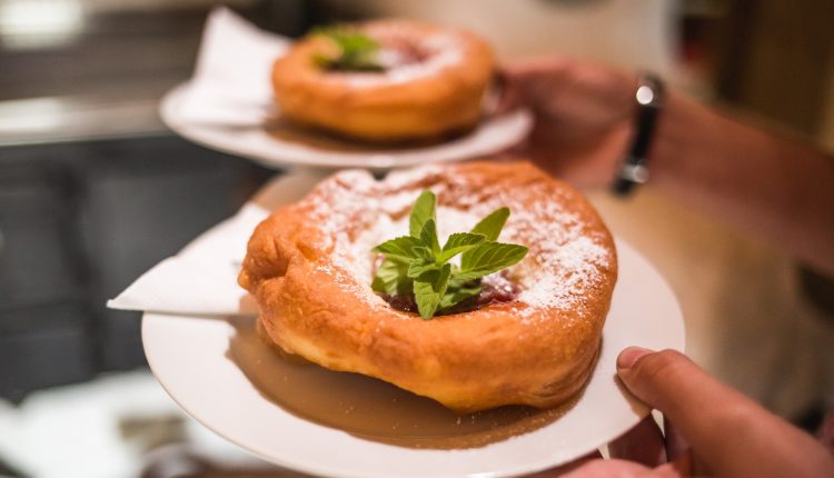 Nahaufnahme von zwei Tellern mit frittiertem Teiggebäck, das mit Puderzucker, Marmelade und Minzblättern belegt ist.